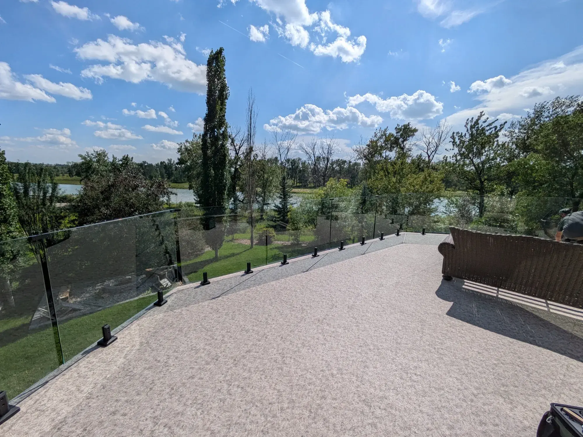 A granite vinyl deck curving away behind frameless glass, lake and summer cloud beyond