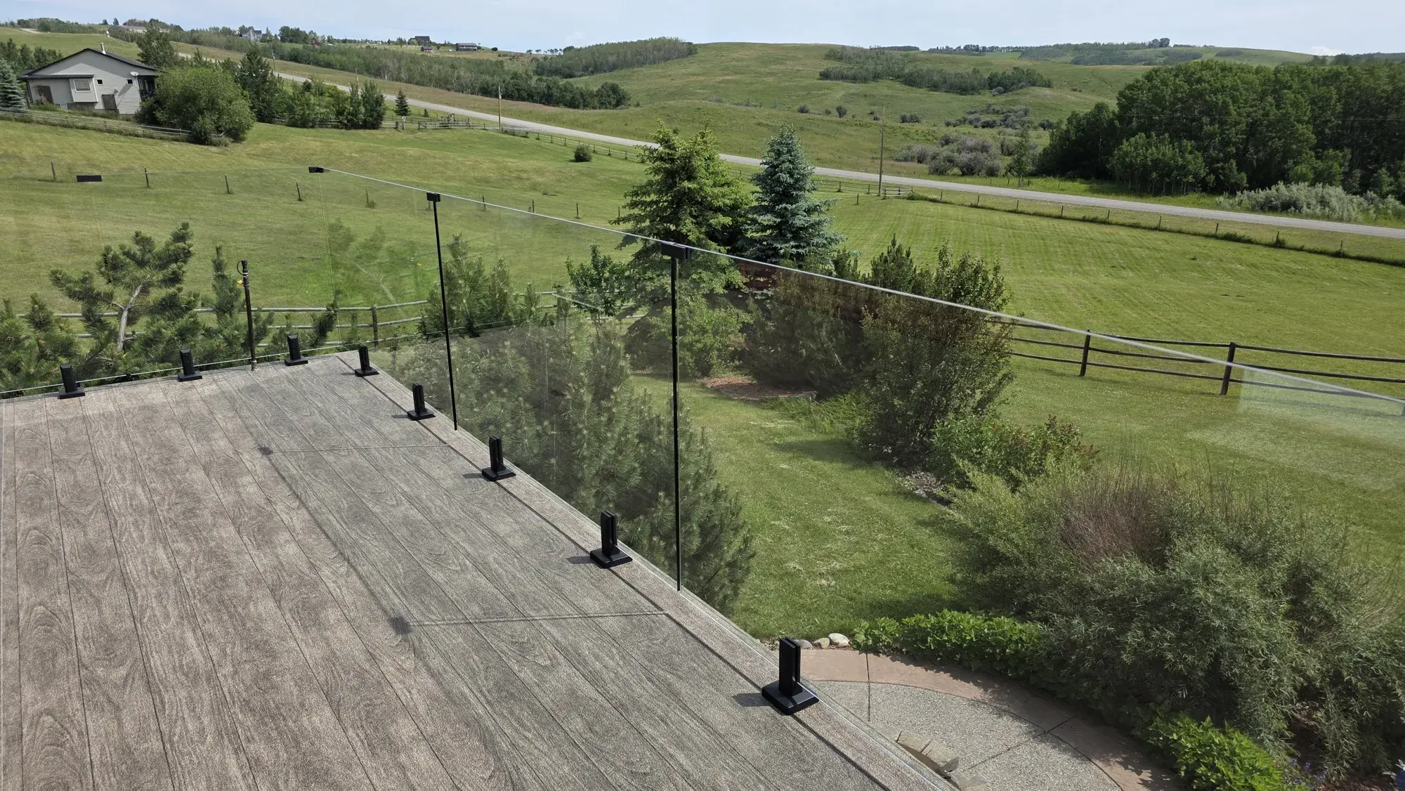 A woodgrain vinyl deck behind frameless glass, green acreage and rolling foothills beyond