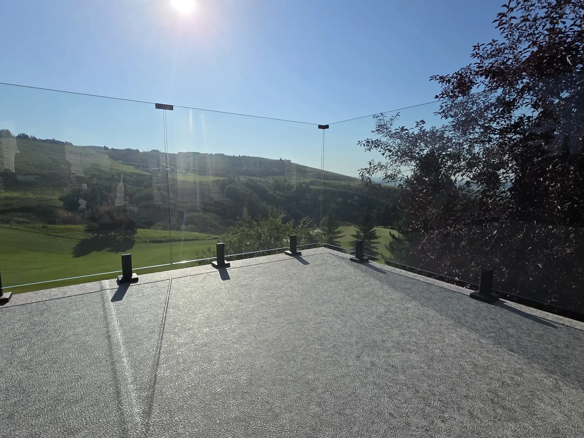 A pale granite vinyl deck behind frameless glass, green foothills under a clear blue sky