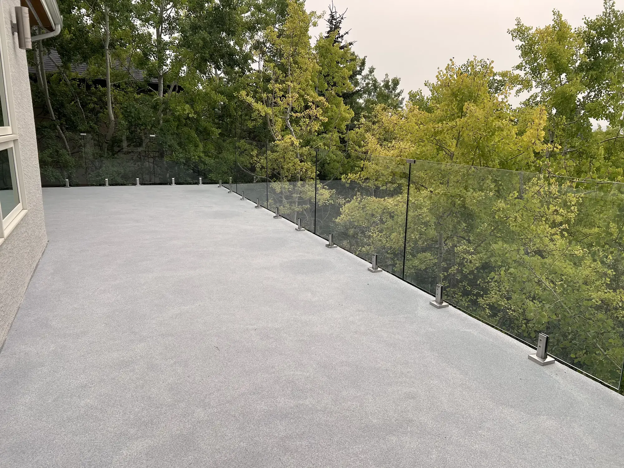 A granite vinyl deck running along the house behind glass railing, green aspens filling the view